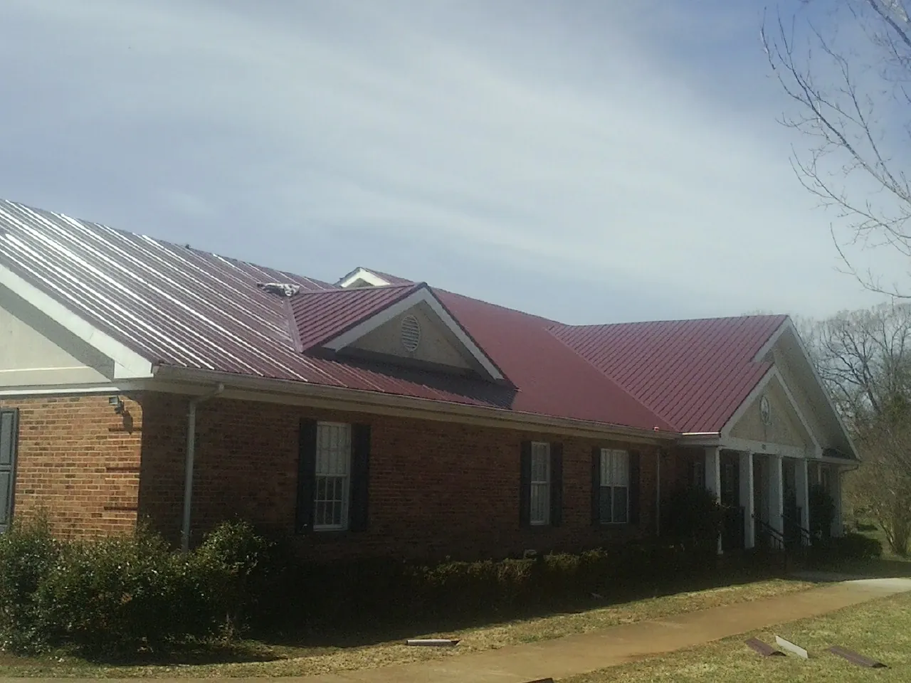 Red metal roof with gabled entries on a long brick building, from a Hail Damage Roof Repair job in Carpentersville