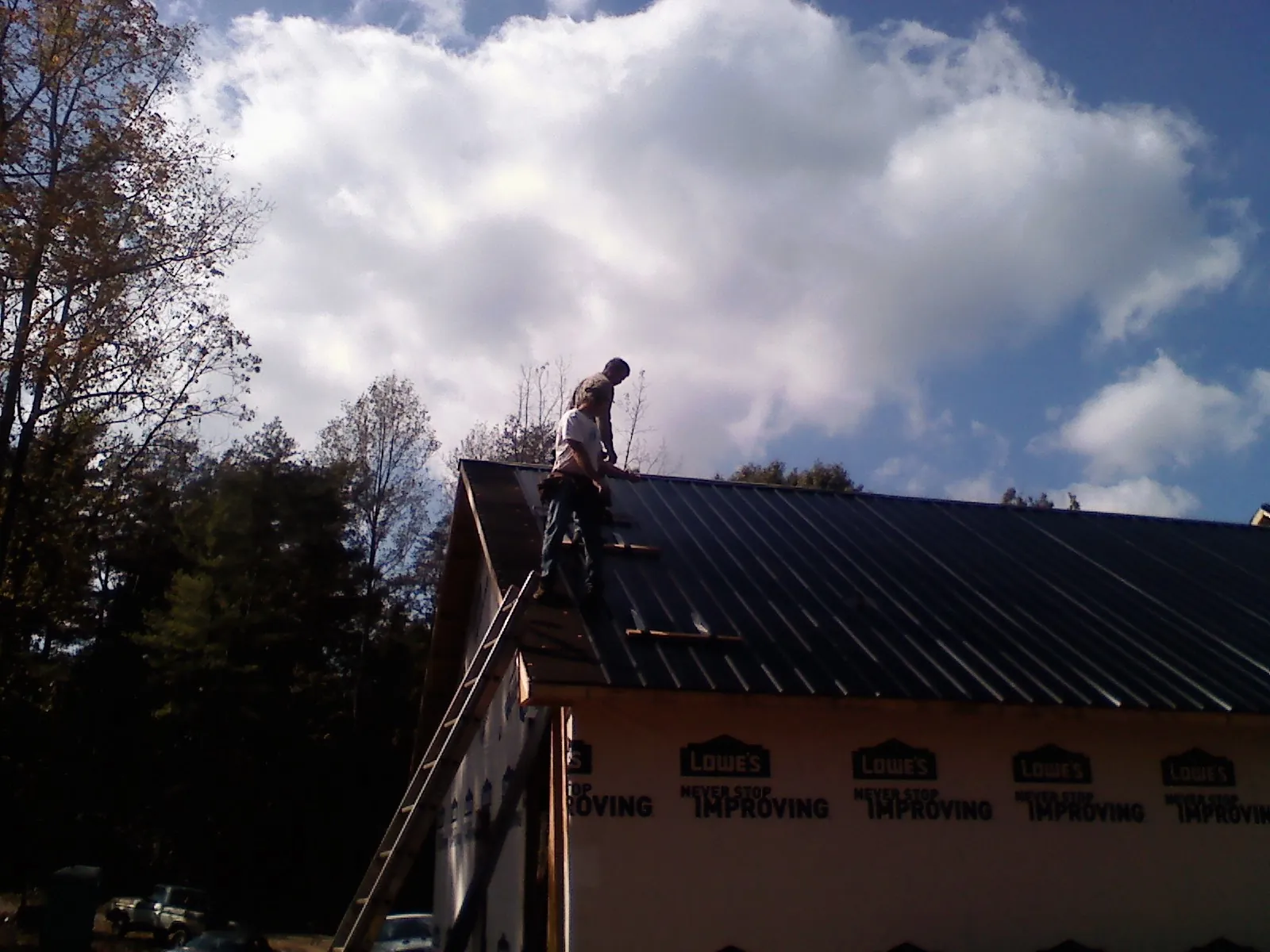 Roofer fastening dark metal panels high against a cloudy sky, from a Roof Inspection job in Carpentersville