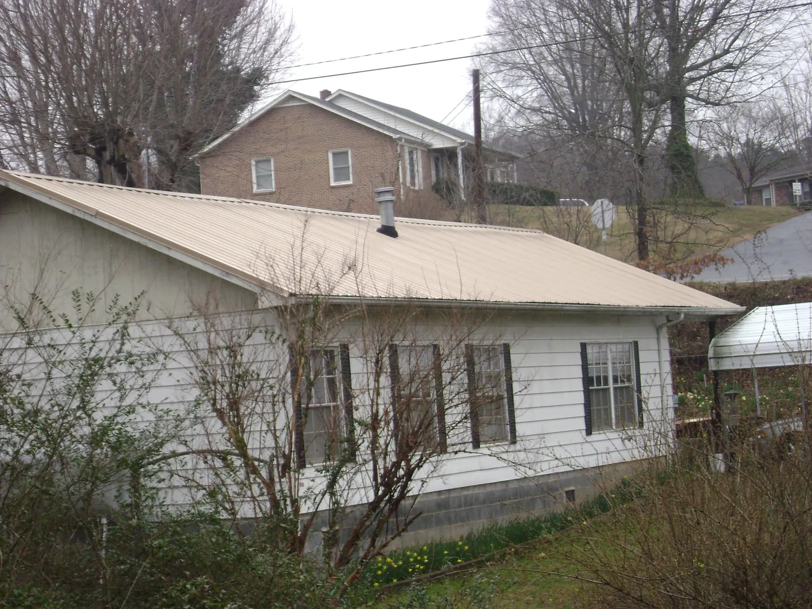 Tan metal roof on a white sided house set into a hillside — Commercial Roofing by Roofing Brothers in Carpentersville